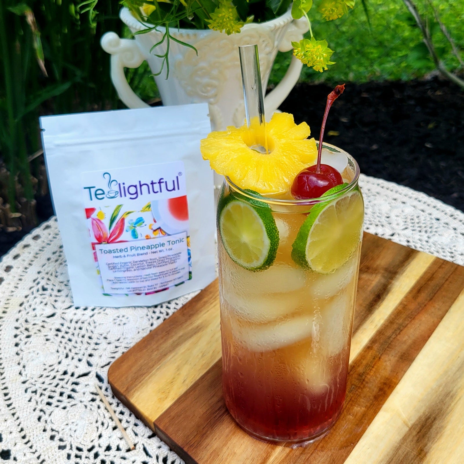 Tropical-themed iced tea with pineapple, cherry, and lime on a wooden board with the Tealightful product in the background.